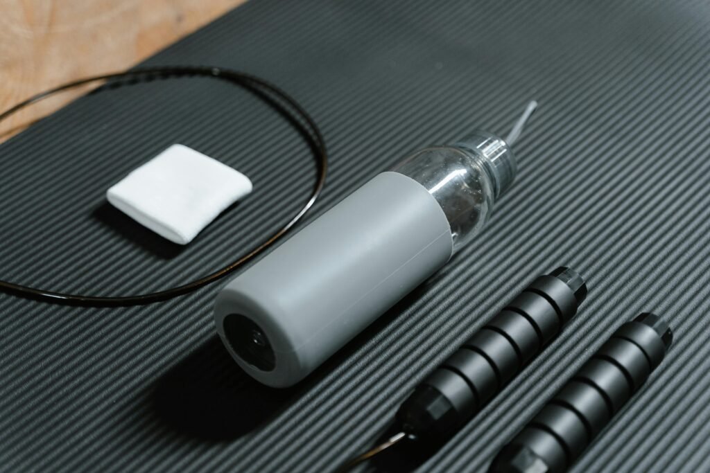 Gray water bottle and jump rope on textured black yoga mat. Indoor workout essentials.